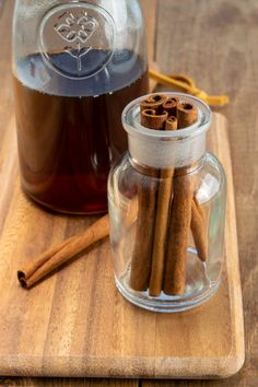 cinnamon sticks are in a glass jar next to a jug of liquid on a wooden cutting board