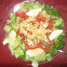 a salad with noodles and vegetables in it on a clear glass plate sitting on a red table cloth