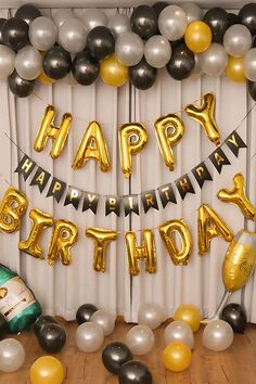 a birthday party with balloons, streamers and champagne bottles on a table in front of a curtain