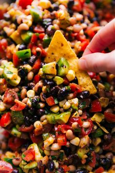 a hand is dipping a tortilla chip into a bowl filled with black beans, corn and avocado