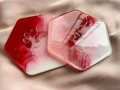 two pieces of red and white glass sitting on top of a bed covered in sheets