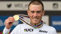 a man holding up a gold medal in his right hand and wearing a white shirt