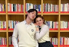 a man and woman standing next to each other in front of bookshelves