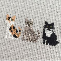 three cross stitch cats sitting next to each other