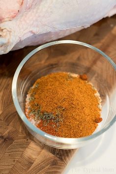 a glass bowl filled with spices on top of a wooden table next to a raw chicken