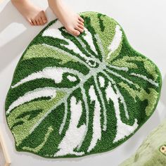 a person standing on a green and white rug next to a plant shaped object with one foot on it