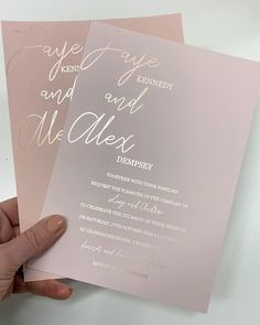 a person holding up two pink and gold wedding cards with writing on the inside of them