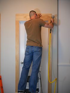 a man standing on a stepladder working on a wooden door with a yellow hose attached to it