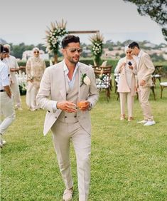 a man in a suit and tie walking through the grass with other men behind him