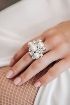 a close up of a person's hand wearing a ring with pearls on it