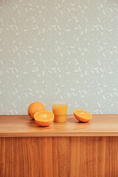 two oranges sitting on top of a wooden counter next to an empty glass cup