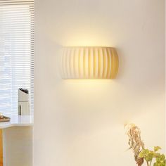 a white wall mounted light next to a potted plant on top of a table