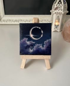 an easel with a painting on it sitting next to a candle and some lights