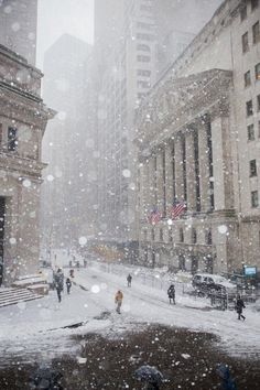 people walking in the snow on a city street with tall buildings and an american flag