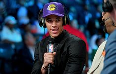 a man with headphones on sitting in front of a microphone and wearing a lakers hat