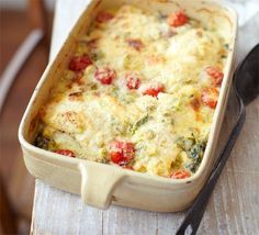 a casserole dish with tomatoes, cheese and spinach in it on a wooden table