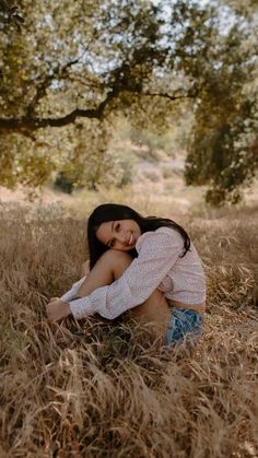 a woman is sitting in the grass with her arms around her head and looking into the distance