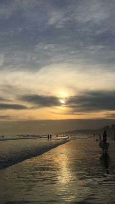 people are walking along the beach as the sun is setting in the sky over the water