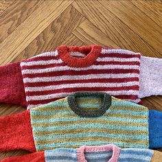 four knitted sweaters laid out on the floor, all in different colors and patterns