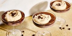 three desserts with chocolate frosting and coffee beans on a table next to wine glasses