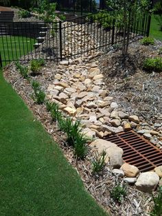 a garden bed with rocks and grass in the foreground, next to a fence