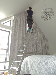 a man standing on a ladder in front of a window next to a white bed