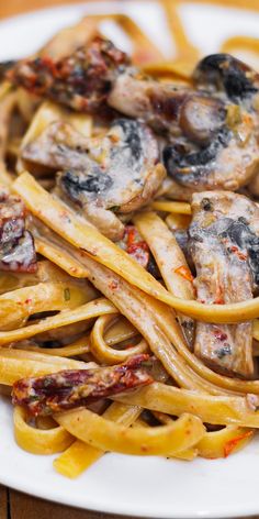 a white plate topped with pasta covered in mushrooms and sauce on top of a wooden table