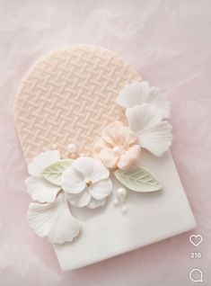 a white box with flowers on it sitting on a pink tableclothed surface next to a heart shaped object