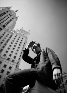 black and white photograph of a man sitting in front of tall buildings