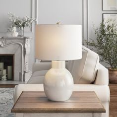 a white table lamp sitting on top of a wooden table in front of a couch