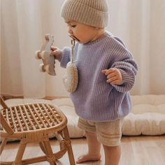 a small child standing in front of a chair and holding a stuffed animal on it's finger