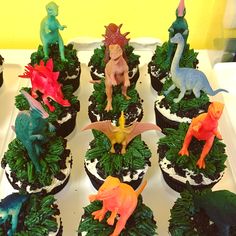 cupcakes decorated with dinosaur figurines on top of green grass and trees