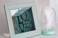 a white feather sitting next to a green frame with the word love spelled in it