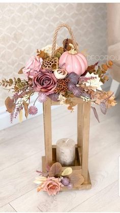 a small wooden lantern with flowers and leaves in it on the floor next to a candle