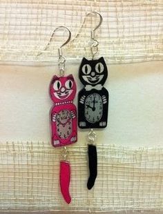 two cats are hanging from the side of a pair of earrings