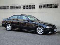 a black car is parked in front of a building with white rims on it