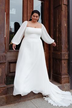 a woman standing in front of a door wearing a white dress