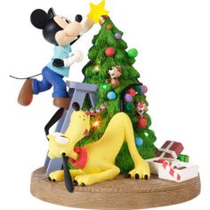 a mickey mouse figurine is decorating a christmas tree with his dog and presents