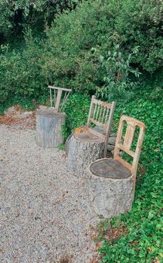 two wooden chairs sitting next to each other on top of a gravel road near trees