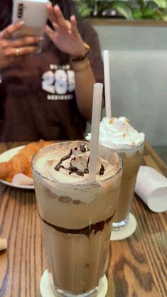 two people sitting at a table with drinks in front of them and one holding a cell phone