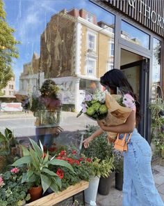 a woman holding flowers in front of a flower shop with her reflection on the window