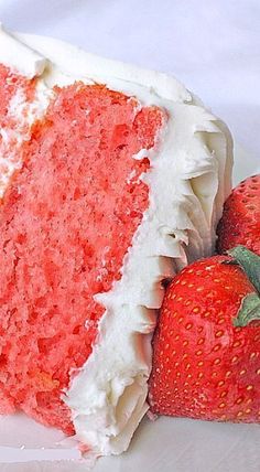 a slice of strawberry cake with white frosting and two strawberries on the side