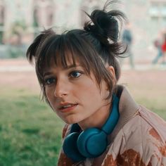 a woman with headphones on her ears in the middle of a grassy park area