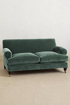 a green couch sitting on top of a floor next to a white wall and wooden legs