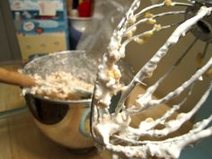 a mixer with white frosting on it and a wooden spoon in front of it