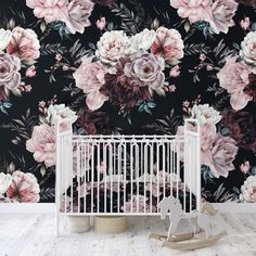 a white crib in front of a floral wallpaper with pink and purple flowers