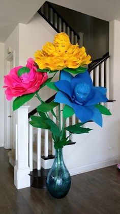 three colorful flowers are in a vase on the floor next to a stair case and railing