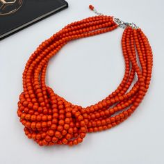 "Embrace your love for vibrant hues with our Orange Knot Necklace. This statement piece showcases the beauty of bold colors with its exuberant orange beads, meticulously knotted to create a distinctive chunky silhouette. This handcrafted necklace is designed to rest comfortably on your collarbone, becoming a focal point of any ensemble. Perfect for special occasions or to infuse your daily wear with a burst of color, this energetic necklace is a must-have for those who like to stand out in the c Orange Beads As A Gift, Orange Beaded Necklaces As Gift, Orange Beaded Necklaces With Wooden Beads For Gifts, Orange Beaded Necklaces With Wooden Beads As Gift, Multi-strand Orange Necklaces For Gifts, Orange Multi-strand Necklaces For Gifts, Orange Multi-strand Beads As Gift, Elegant Orange Beaded Necklace With Wooden Beads, Orange Multi-strand Beaded Necklaces