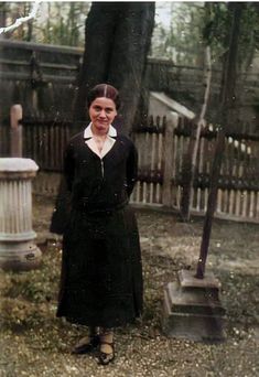 an old photo of a woman standing in front of a tree