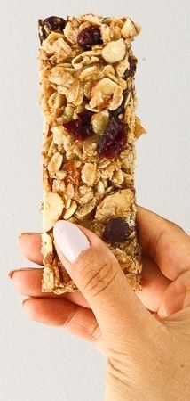 a person holding up a granola bar with nuts and cranberries on it